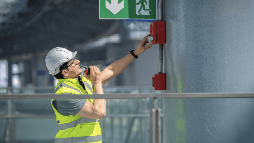 man in safety best talking on walkie talkie while looking at red emergency system